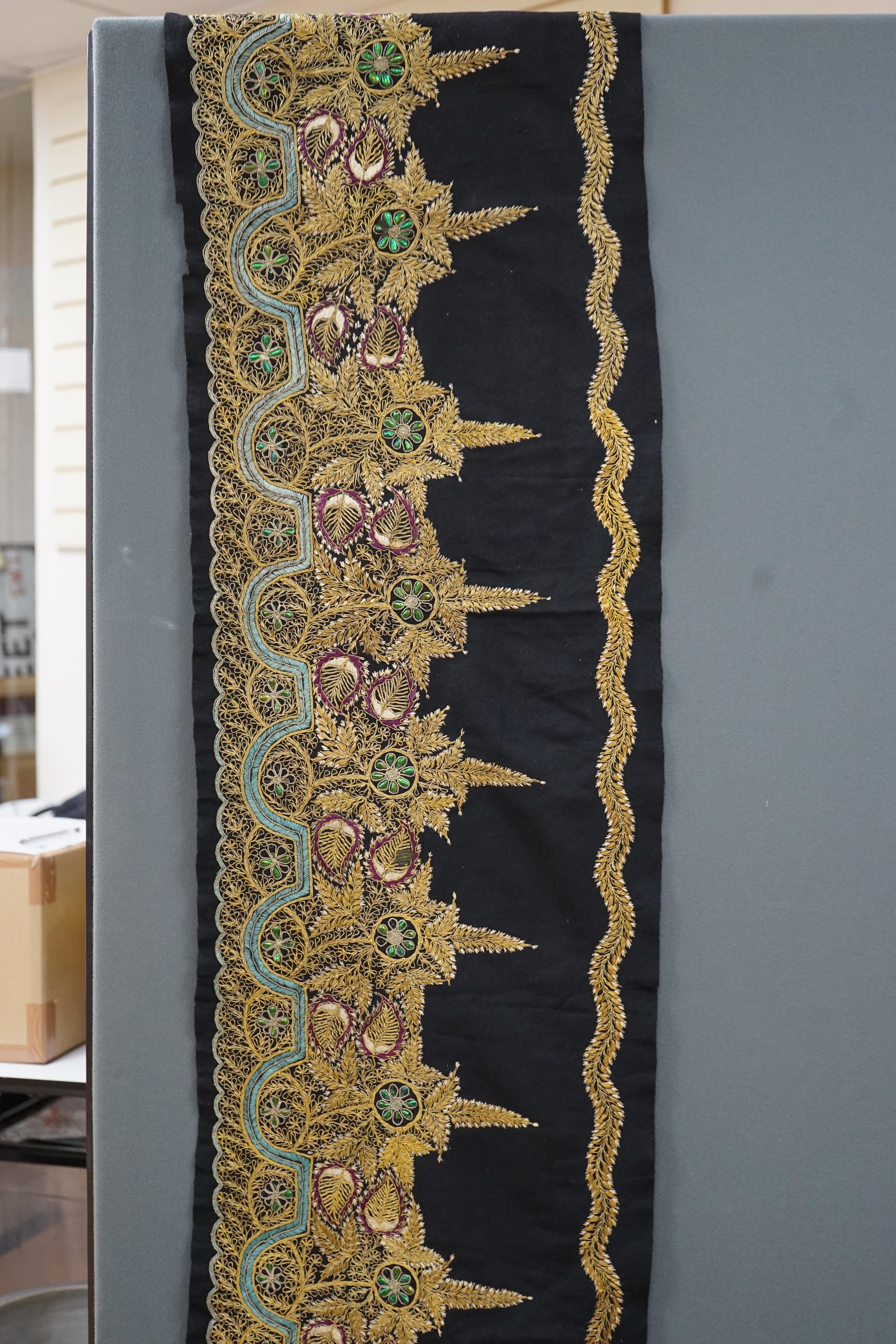 An Indian black felt panel embroidered with mostly gold thread, some coloured silks and beetle wing ornamentation, possibly a border to a larger panel, 256cm long. Condition - good